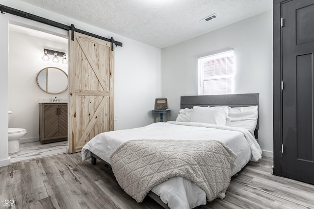 bedroom with ensuite bath, sink, a barn door, light hardwood / wood-style floors, and a textured ceiling