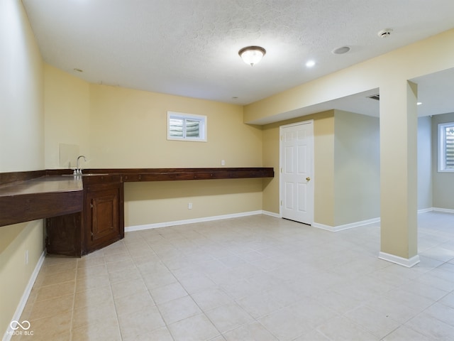 basement featuring a textured ceiling, a healthy amount of sunlight, and sink