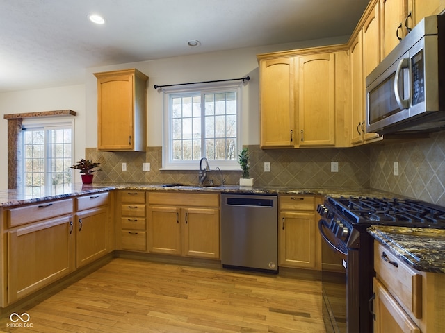 kitchen with appliances with stainless steel finishes, a wealth of natural light, dark stone counters, sink, and light hardwood / wood-style floors