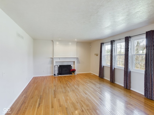 unfurnished living room featuring a fireplace, a textured ceiling, and light wood-type flooring