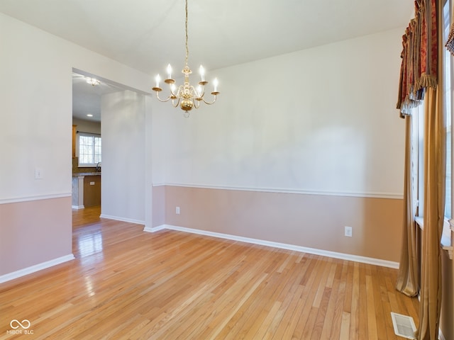 empty room featuring an inviting chandelier and light hardwood / wood-style flooring