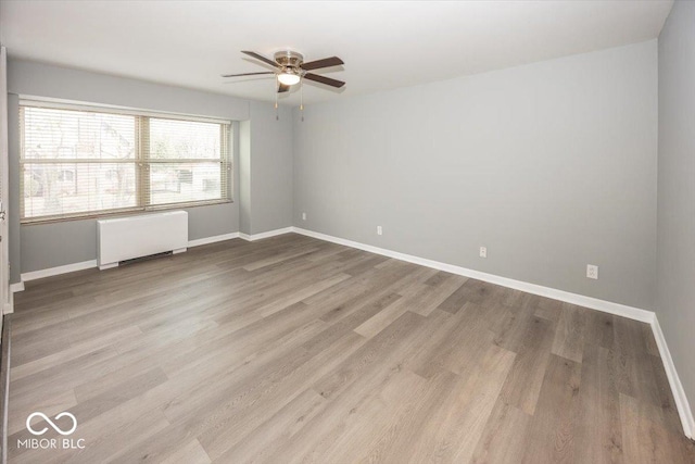 empty room featuring ceiling fan, light wood-type flooring, and radiator heating unit