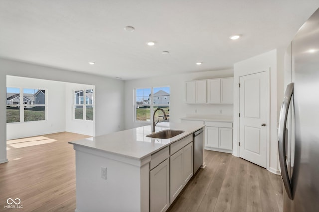 kitchen with appliances with stainless steel finishes, sink, a center island with sink, light hardwood / wood-style floors, and white cabinetry