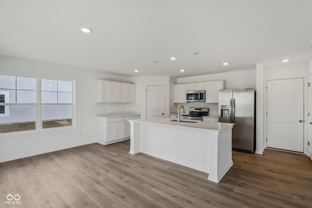 kitchen with light hardwood / wood-style floors, white cabinetry, stainless steel appliances, and a kitchen island with sink