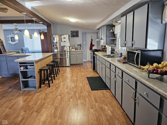 kitchen with pendant lighting, lofted ceiling, sink, light wood-type flooring, and stainless steel appliances