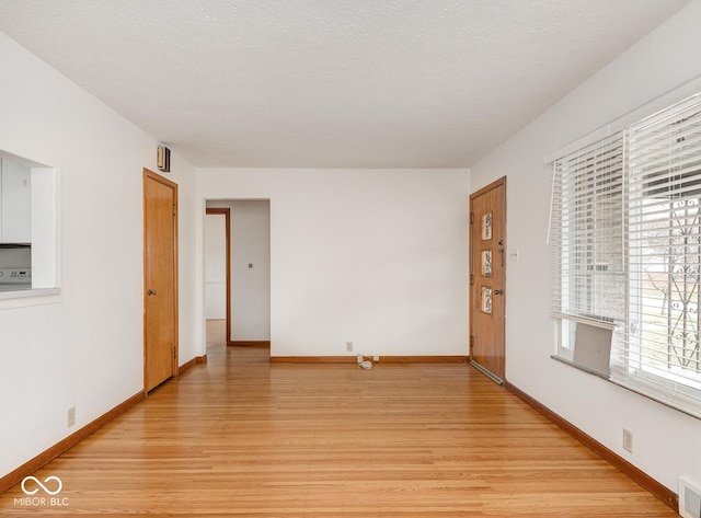 empty room with light wood-type flooring and a textured ceiling