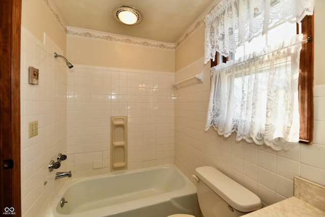 bathroom featuring tiled shower / bath, toilet, and tile walls