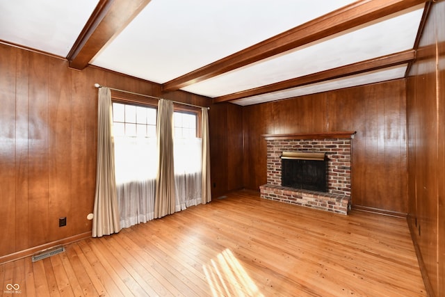 unfurnished living room featuring a fireplace, beam ceiling, light hardwood / wood-style floors, and wood walls