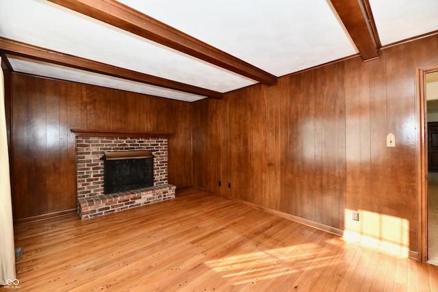 unfurnished living room with wood walls, beam ceiling, light wood-type flooring, and a brick fireplace