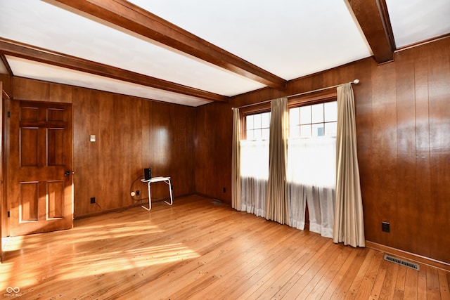 unfurnished room with beam ceiling, wood walls, and light hardwood / wood-style flooring