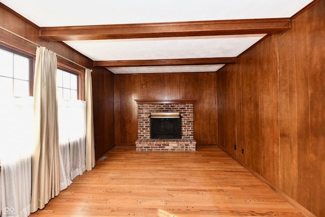 unfurnished living room featuring a brick fireplace, beam ceiling, wooden walls, and light hardwood / wood-style flooring