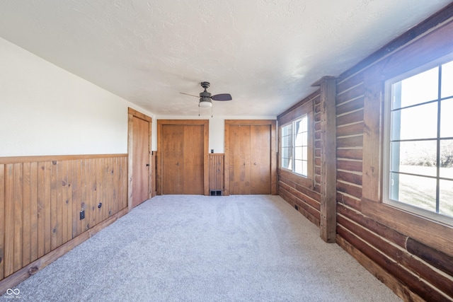 carpeted spare room with wooden walls, ceiling fan, and a textured ceiling