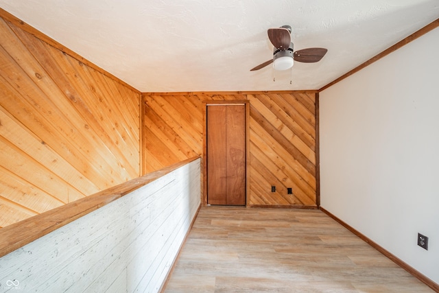 spare room with ceiling fan, crown molding, wooden walls, and light hardwood / wood-style flooring