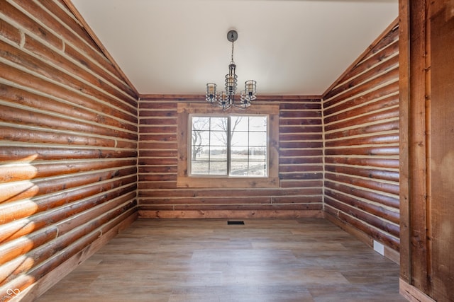 spare room with log walls, wood-type flooring, lofted ceiling, and an inviting chandelier