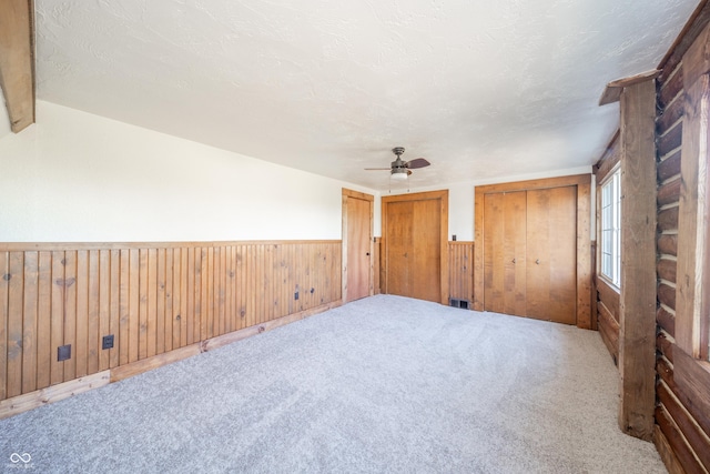 empty room with wood walls, carpet floors, a textured ceiling, and ceiling fan