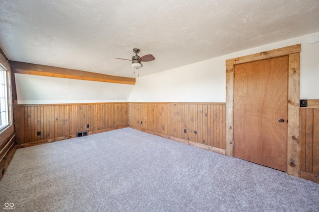 carpeted spare room featuring a textured ceiling, ceiling fan, and wood walls