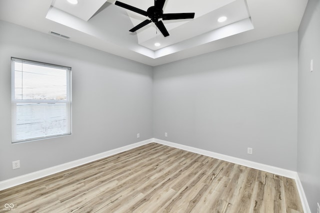 empty room with light hardwood / wood-style floors, ceiling fan, and a tray ceiling