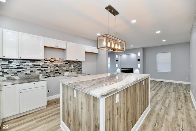 kitchen with white cabinetry, light stone counters, pendant lighting, a kitchen island, and light wood-type flooring