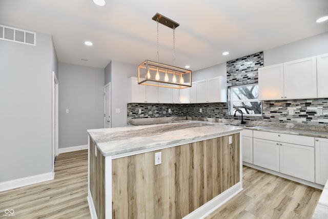 kitchen with light stone counters, a center island, pendant lighting, and light wood-type flooring