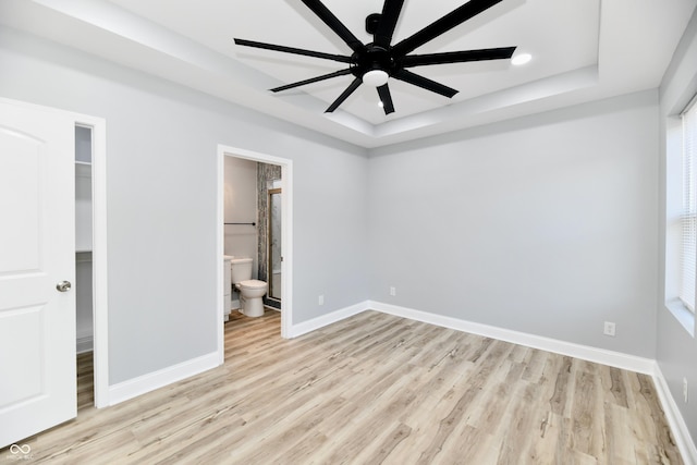 unfurnished bedroom featuring ceiling fan, a raised ceiling, light wood-type flooring, and ensuite bath