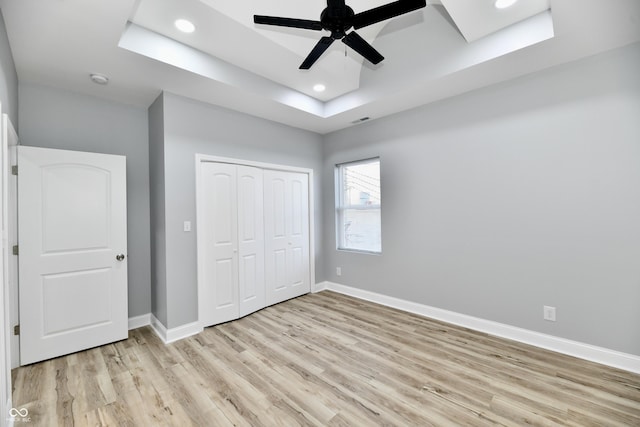 unfurnished bedroom featuring ceiling fan, light hardwood / wood-style floors, a tray ceiling, and a closet