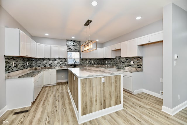 kitchen featuring white cabinetry, a center island, light hardwood / wood-style floors, and decorative light fixtures