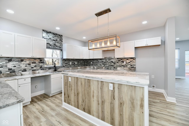 kitchen with light stone countertops, light wood-type flooring, white cabinets, a center island, and hanging light fixtures