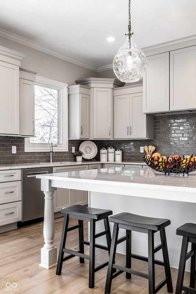 kitchen with stainless steel dishwasher, backsplash, pendant lighting, light hardwood / wood-style floors, and a kitchen bar