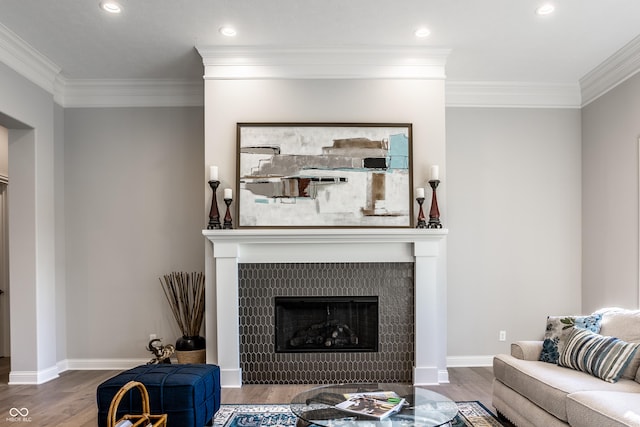 living room with wood-type flooring, ornamental molding, and a tiled fireplace