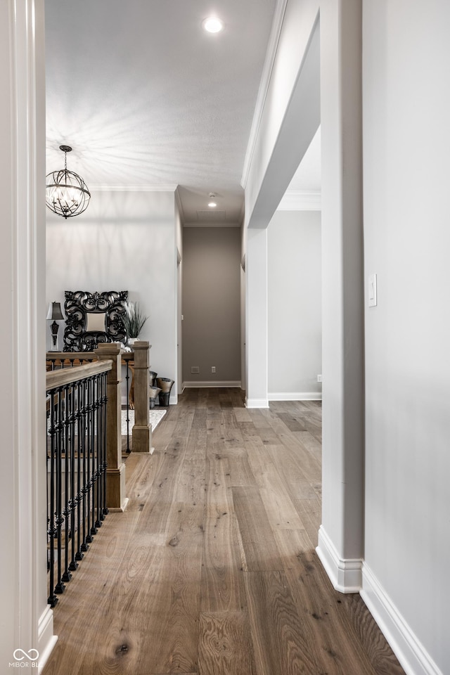 corridor with crown molding, light hardwood / wood-style flooring, and a notable chandelier