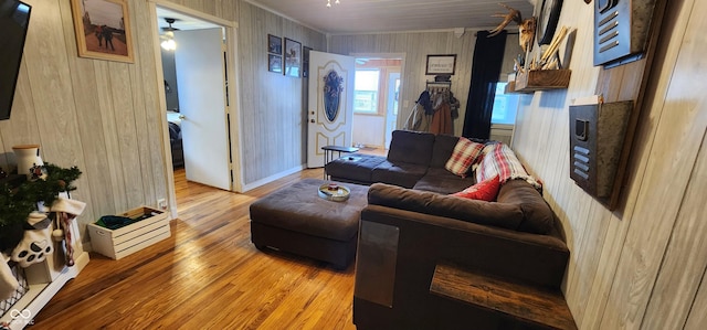 living room with ceiling fan, wood-type flooring, and wood walls