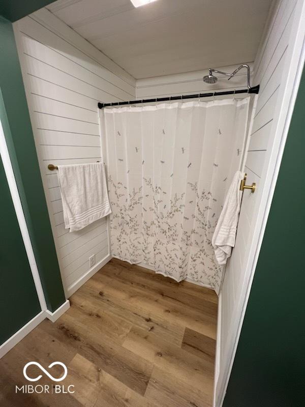 bathroom with a shower with shower curtain, wooden walls, and hardwood / wood-style floors