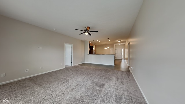 unfurnished living room with ceiling fan with notable chandelier and dark carpet