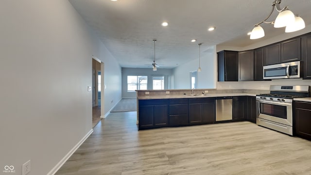 kitchen with kitchen peninsula, hanging light fixtures, ceiling fan with notable chandelier, appliances with stainless steel finishes, and sink