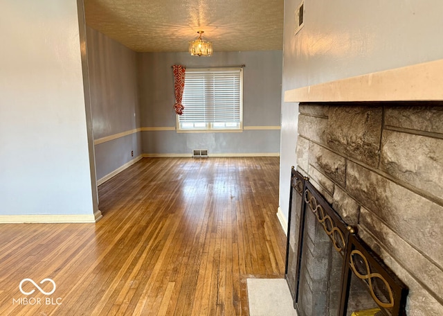 unfurnished living room featuring hardwood / wood-style flooring, an inviting chandelier, a fireplace, and a textured ceiling