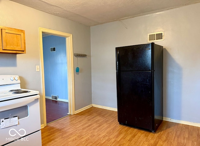 kitchen with white electric range, light wood-type flooring, a textured ceiling, and black fridge