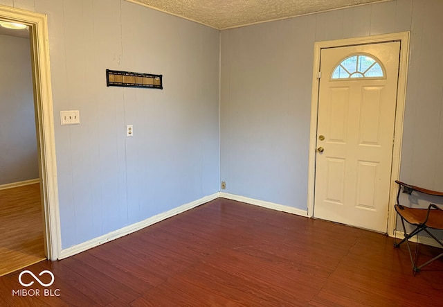 foyer featuring a textured ceiling, wooden walls, and dark wood-type flooring