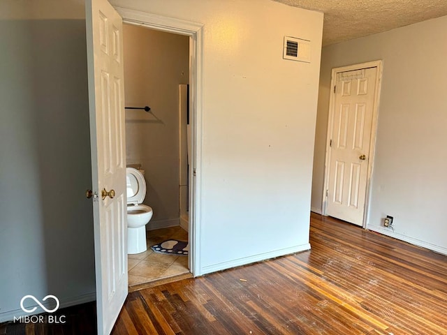 unfurnished bedroom with a textured ceiling, connected bathroom, a closet, and dark hardwood / wood-style floors