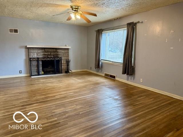 unfurnished living room with a fireplace, ceiling fan, hardwood / wood-style floors, and a textured ceiling