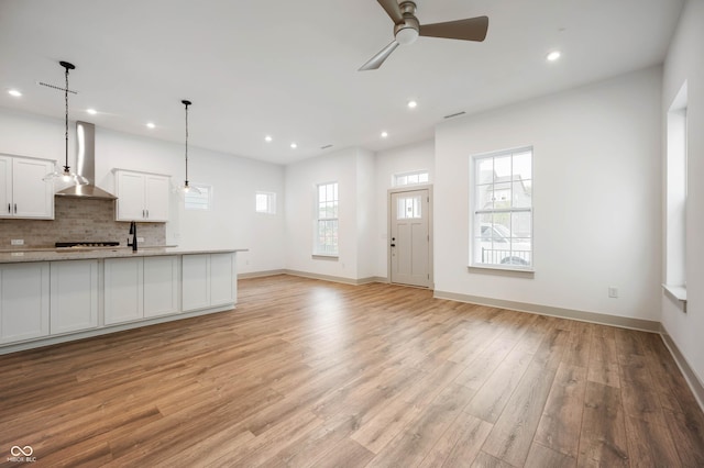 unfurnished living room featuring plenty of natural light, ceiling fan, light wood-type flooring, and sink