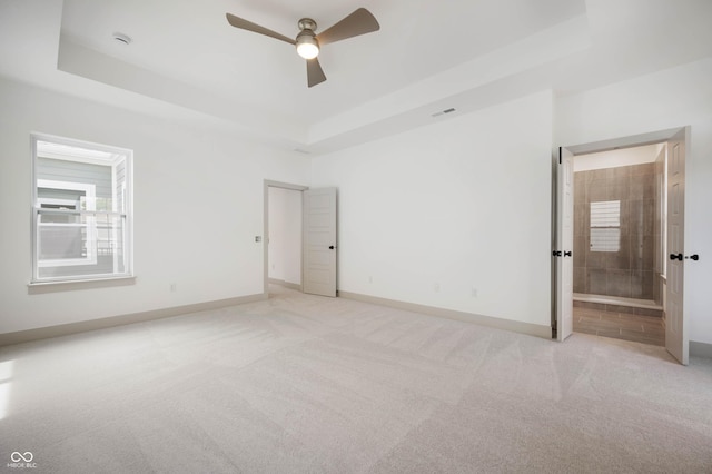 unfurnished bedroom with a raised ceiling, ceiling fan, light colored carpet, and connected bathroom