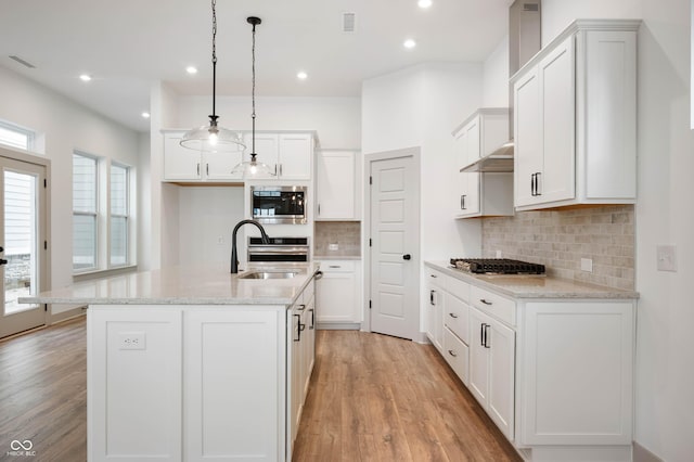 kitchen with pendant lighting, stainless steel appliances, white cabinetry, and a center island with sink