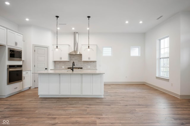 kitchen featuring white cabinetry, a center island with sink, stainless steel appliances, and wall chimney range hood