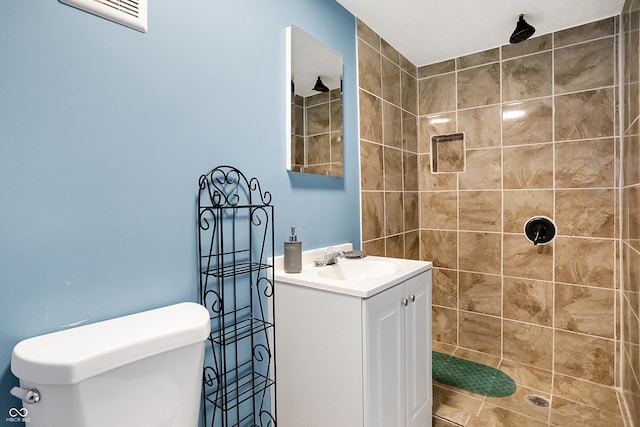 bathroom featuring a tile shower, vanity, and toilet