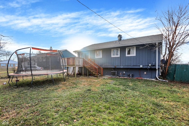 back of property featuring a lawn, a wooden deck, and a trampoline