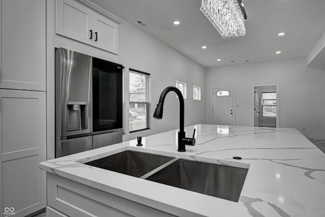 kitchen featuring stainless steel refrigerator with ice dispenser, light stone counters, a notable chandelier, and sink