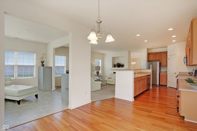 kitchen featuring light wood-type flooring, stainless steel appliances, decorative light fixtures, a chandelier, and a kitchen island