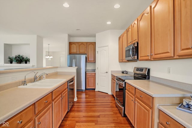 kitchen featuring light wood-type flooring, stainless steel appliances, sink, pendant lighting, and a chandelier