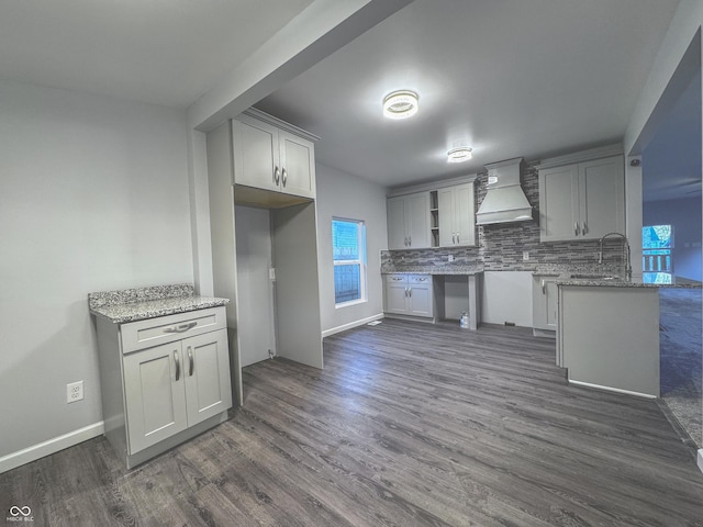 kitchen with kitchen peninsula, decorative backsplash, light stone counters, dark hardwood / wood-style flooring, and custom range hood