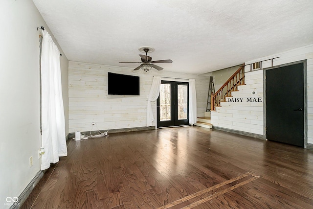 interior space with french doors, a textured ceiling, ceiling fan, wooden walls, and dark wood-type flooring